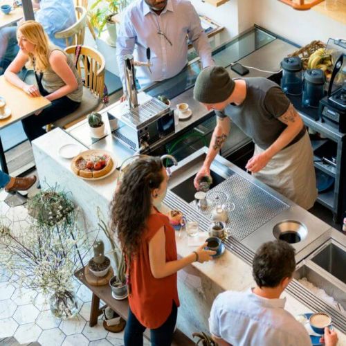 Busy café with baristas preparing drinks behind the counter and customers engaging at tables, illustrating effective restaurant marketing tactics that enhance in-store experience and customer retention.