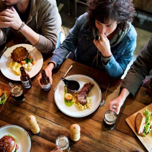 Group of diners sharing craft beer and plated meals at a rustic restaurant table, illustrating the role of social dining experiences in boosting a restaurant’s online presence and digital engagement.