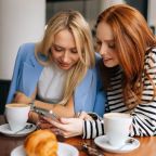 Two women in a café sharing content on a phone – illustrating dark social and private sharing for Hospitality Marketing Hub.